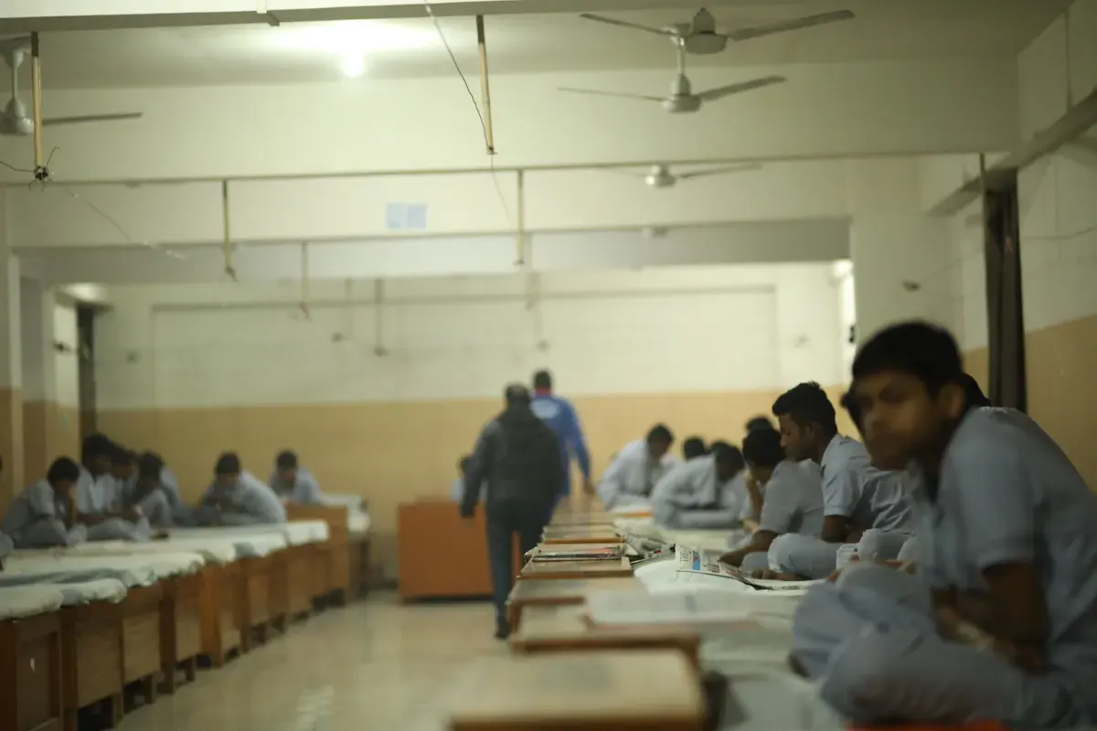 Boarders sitting on their beds in the hostel dormitory as the housemaster walks through
