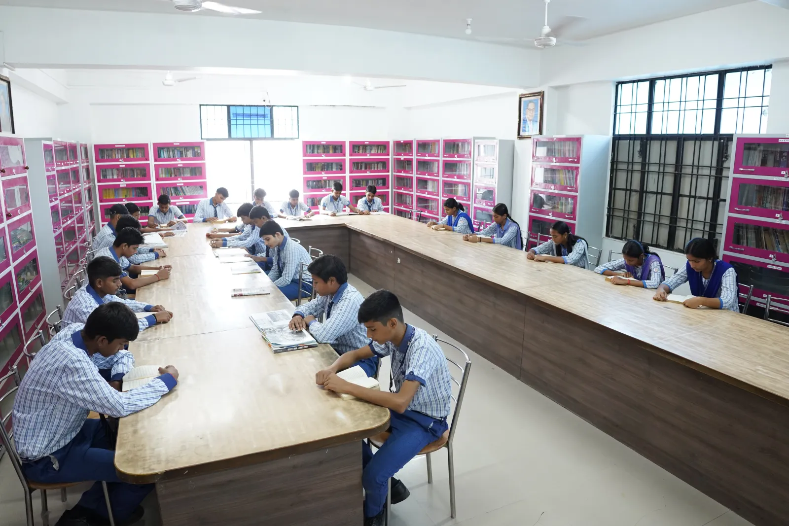 Students reading at long tables in the school library, lined with book cabinets