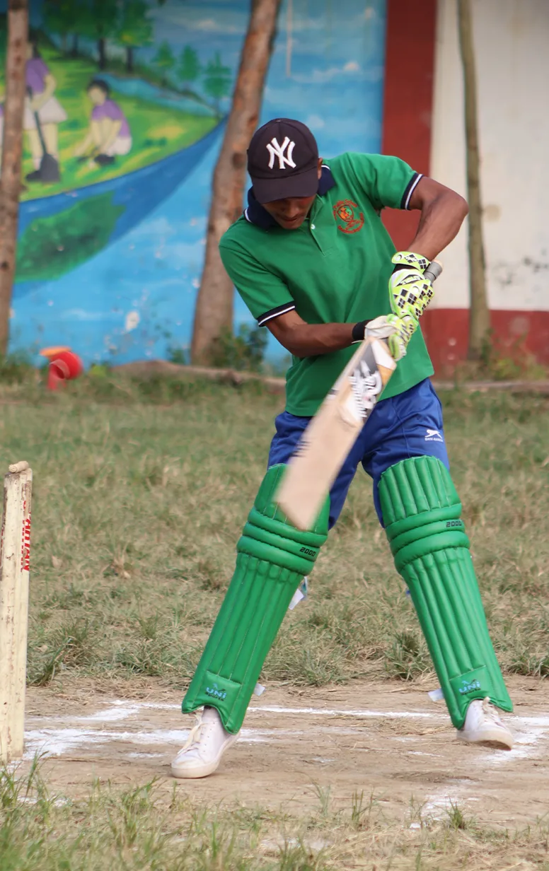 A batter in the green house kit playing a shot at the crease