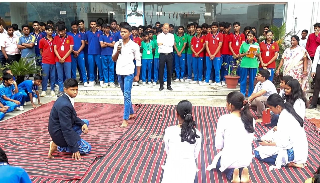 Students performing a street play in the school courtyard as their schoolmates watch